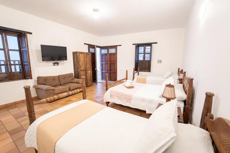 Habitación San Antonio con tres camas, sofá, televisor y puertas de madera