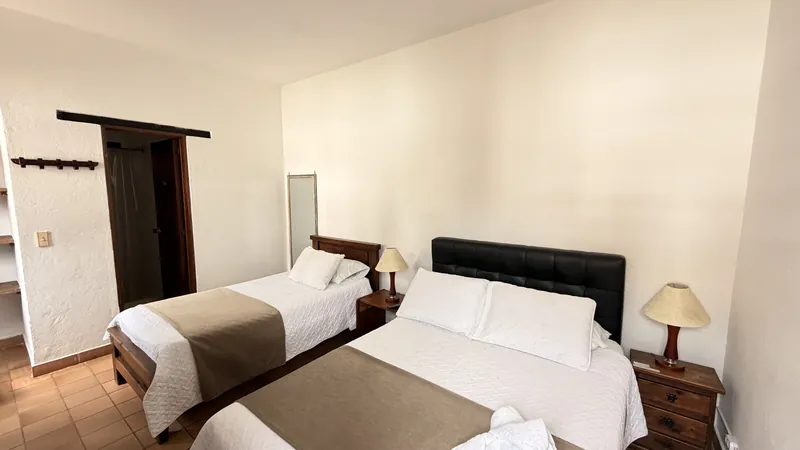 Habitación San Miguel con cama doble de cabecero tapizado, cama sencilla y puerta de madera