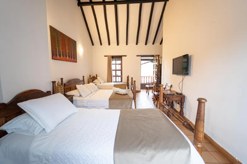 Habitación San Nicolás con tres camas de madera, televisor y puerta al balcón