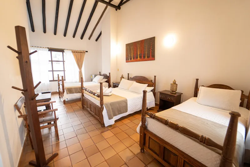 Habitación San Nicolás con camas talladas, minibar junto a la ventana y cuadro de árboles